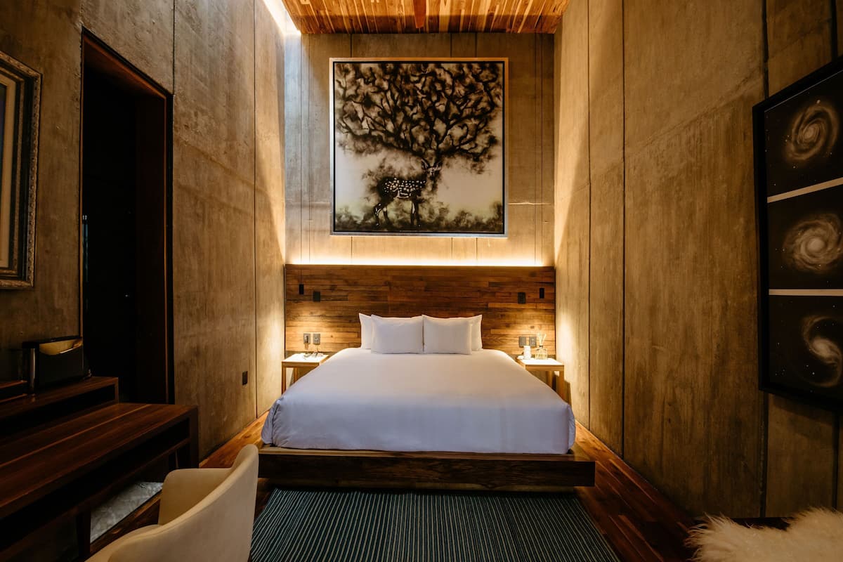 Un dormitorio moderno con una cama grande, cabecera de madera y un cuadro colgado en la pared que representa un árbol.