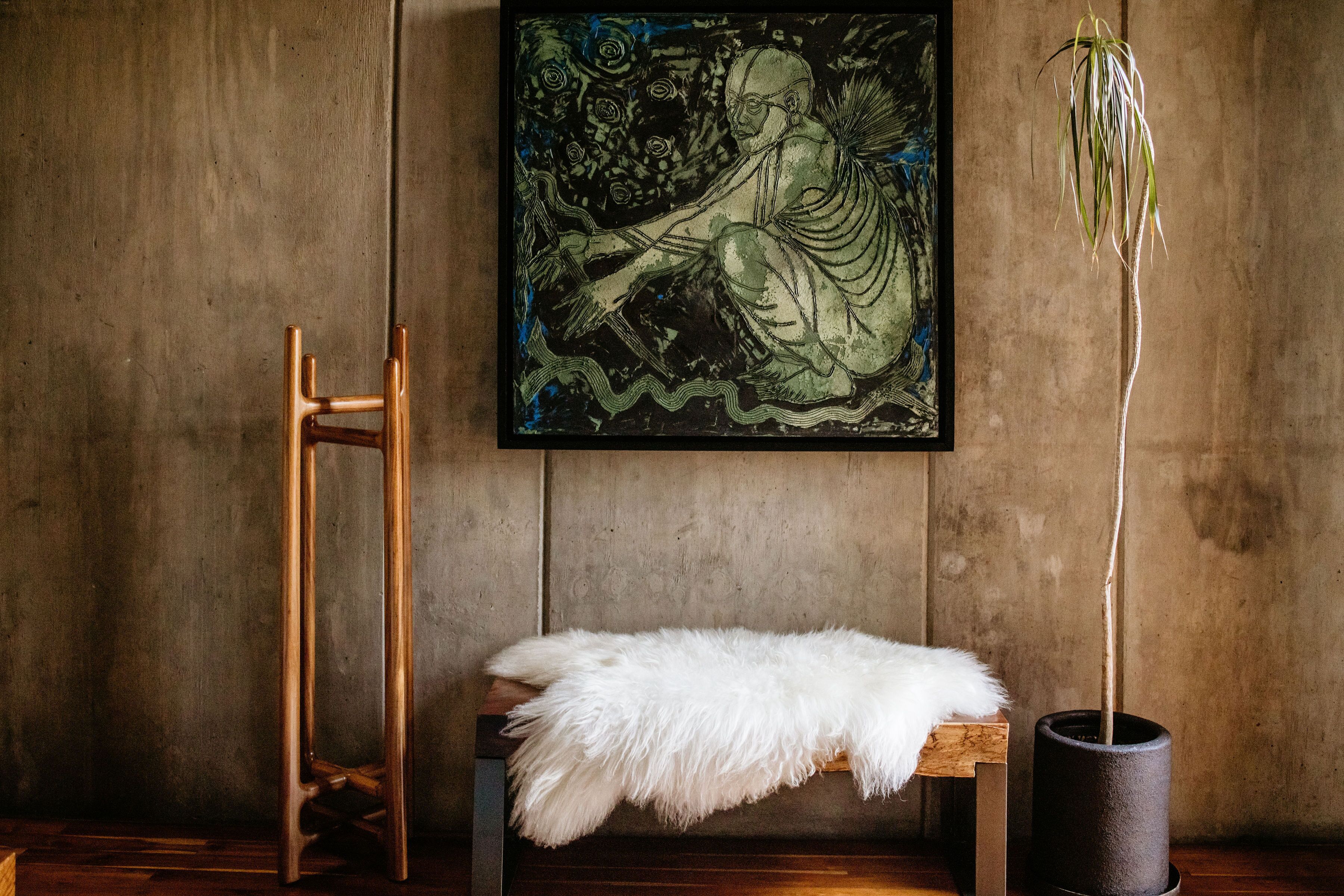 Une pièce comprenant une chaise en bois, un banc recouvert d’un plaid en fausse fourrure blanche, une œuvre d’art encadrée et une plante en pot.