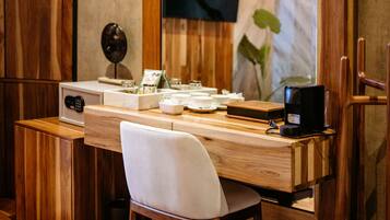 Un escritorio de madera con un espejo grande, una silla, una cafetera y un televisor montado en la pared.