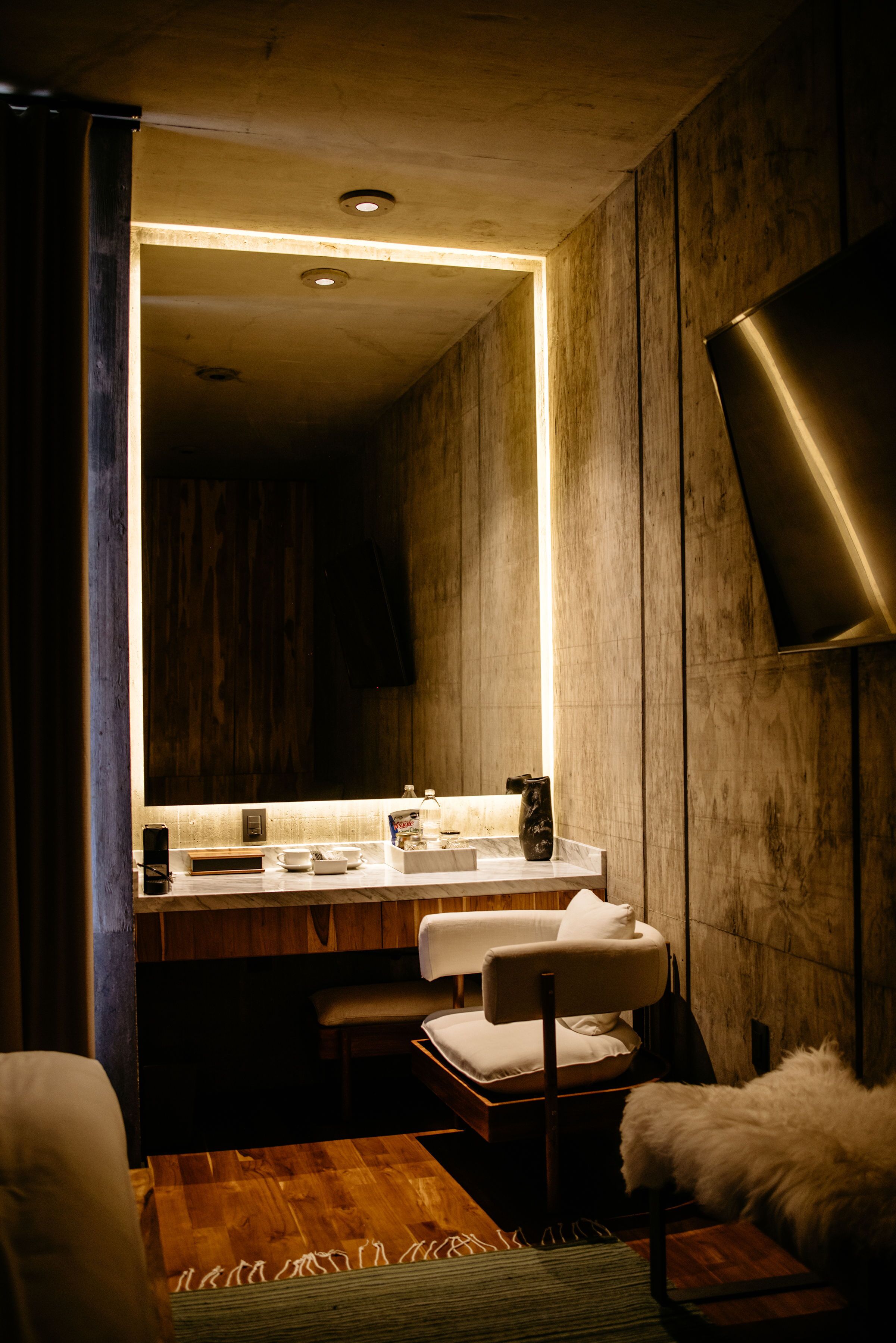 Un baño moderno con tocador de madera, una silla blanca y un espejo grande.