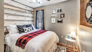 Une chambre à coucher avec un lit, un ventilateur de plafond, une petite table avec une lampe et des tableaux encadrés accrochés au mur.