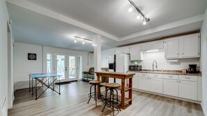 Una cocina amplia con armarios blancos, una mesa de comedor de madera con taburetes y una mesa de ping pong.