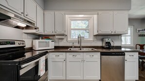 Una cocina con armarios blancos, microondas, lavavajillas y estufa.