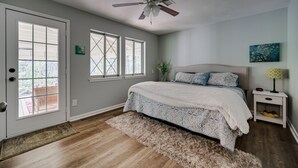 Un dormitorio con cama, ventilador de techo, mesita de noche, ventana y puerta.
