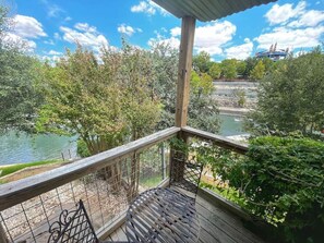 Eine Holzterrasse mit Metallgeländer, mit Blick auf einen Fluss und Bäume.