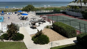 Een tennisbaan met een zwembad, palmbomen en uitzicht op de oceaan.