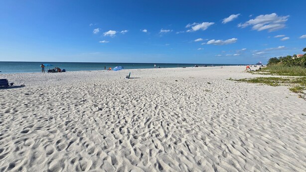 Een breed zandstrand met heldere blauwe lucht en een rustige zee.