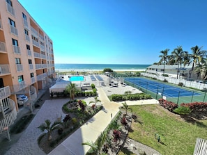 A hotel with a pool, tennis court, and beach view.