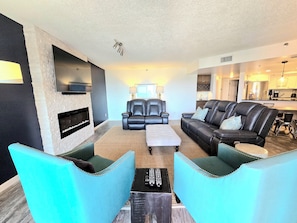 A living room with a fireplace, two leather sofas, a coffee table, and a kitchen in the background.