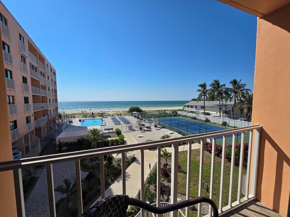 A balcony with a view of a swimming pool, beach, and ocean.