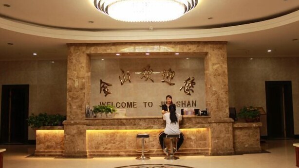 A reception area with a marble wall, a chandelier, and a welcome sign. - Jinshan Hotel (Dunhuang)