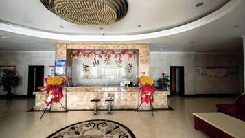 A hotel reception area with a marble counter, two chairs, and a chandelier.