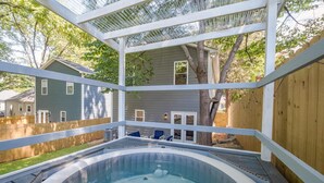 Un bain à remous dans un jardin, avec une terrasse en bois et une maison en arrière-plan.