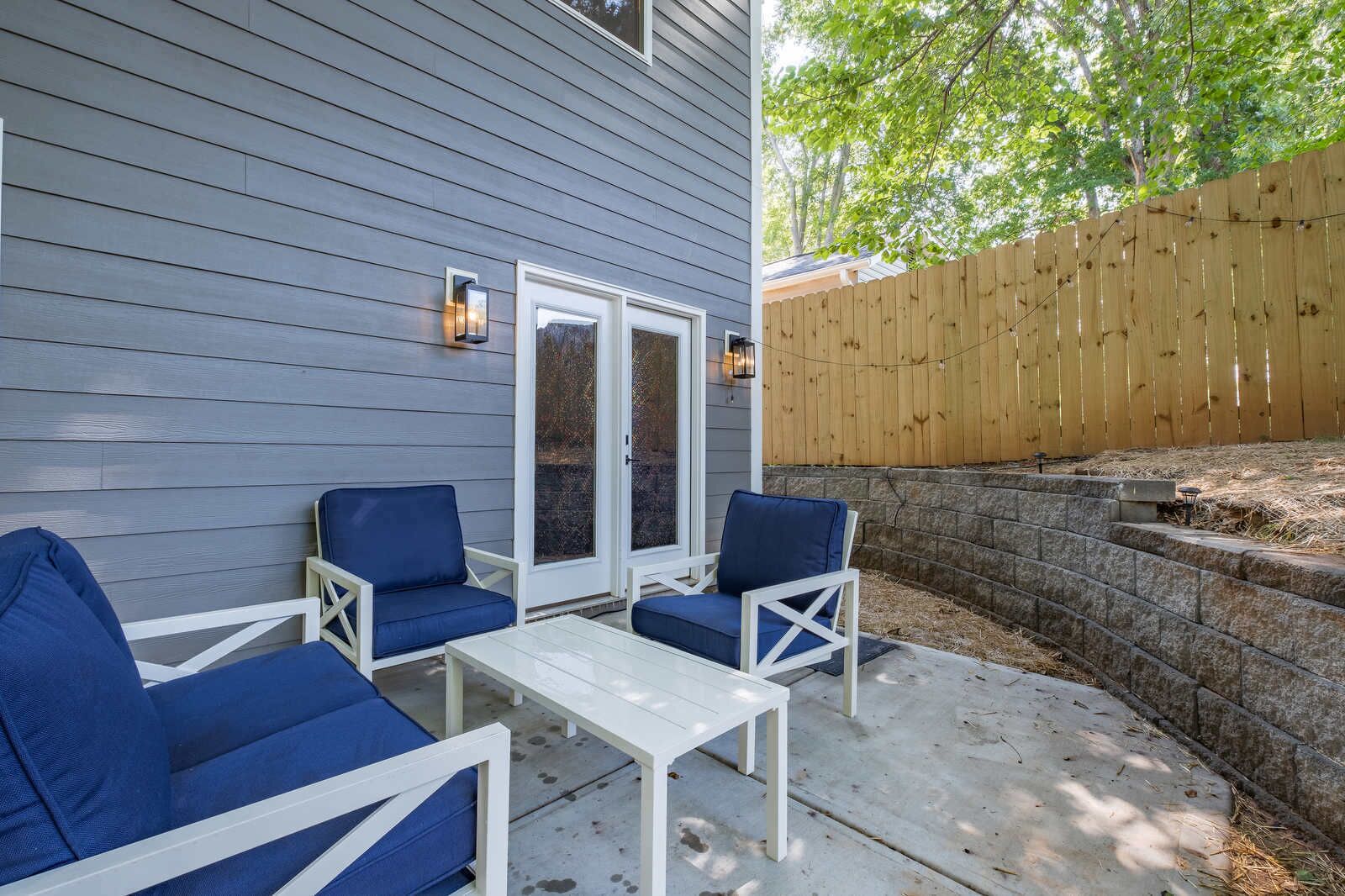 Une terrasse extérieure avec deux chaises bleues dotées de coussins et une table blanche, une clôture en bois et un mur en pierre.