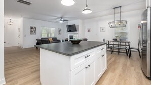 Une cuisine moderne avec des meubles blancs, un îlot central et un coin repas comprenant une table et des chaises.