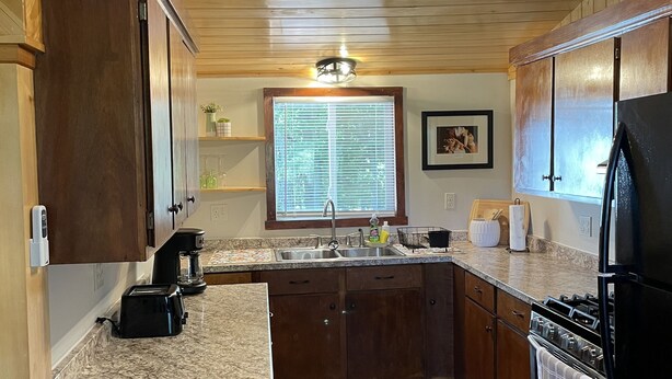 Una cocina con armarios de madera, encimeras de granito, un refrigerador negro, una estufa y una ventana con persianas.