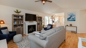 Un salon doté d’une cheminée, d’un ventilateur de plafond et d’un coin repas avec une cuisine en arrière-plan.