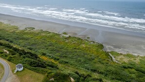 Vue aérienne d’une zone côtière avec une plage, une végétation luxuriante et une petite construction près d’une route.