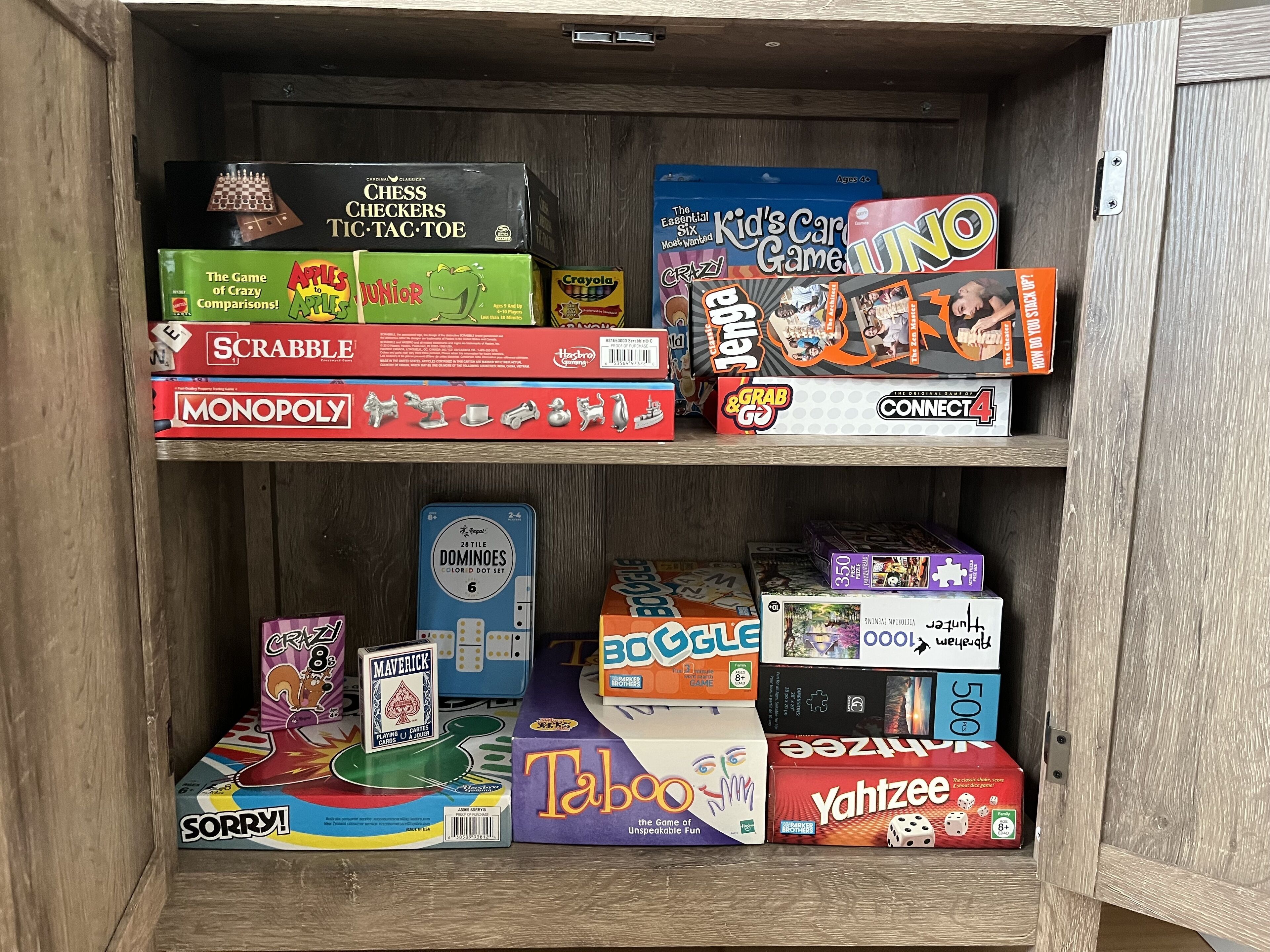 A wooden cabinet with various board games organized on shelves.