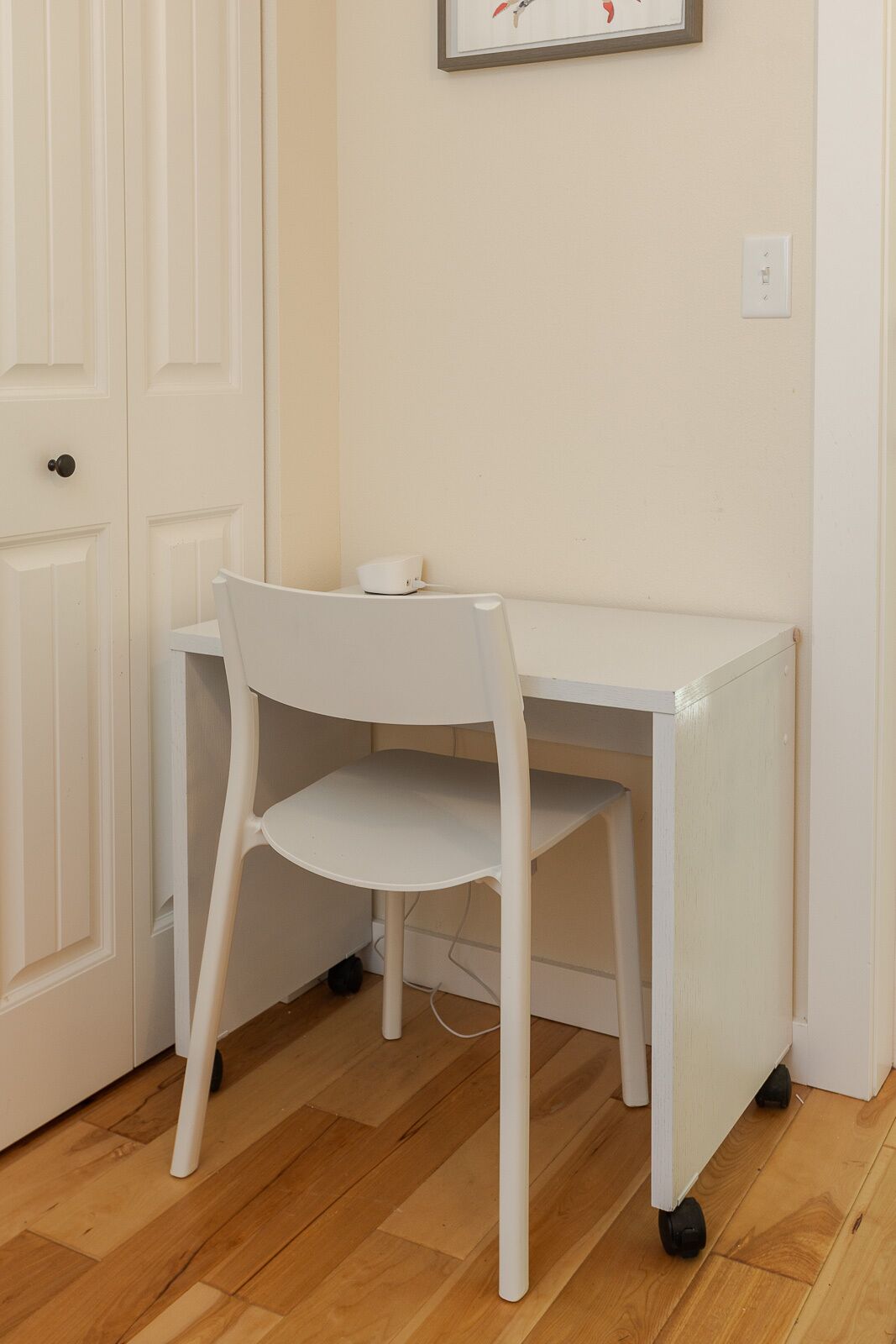 A white desk with a chair in a room with wooden flooring and a white door.
