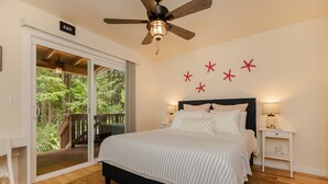 Une chambre avec un lit, un ventilateur de plafond, une table de chevet, une lampe et une vue sur l’extérieur grâce à une porte-fenêtre coulissante.