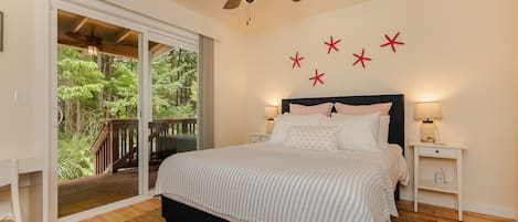 Ein Schlafzimmer mit einem Bett, einem Deckenventilator, einem Nachttisch, einer Lampe und Blick ins Freie durch eine Glasschiebetür.