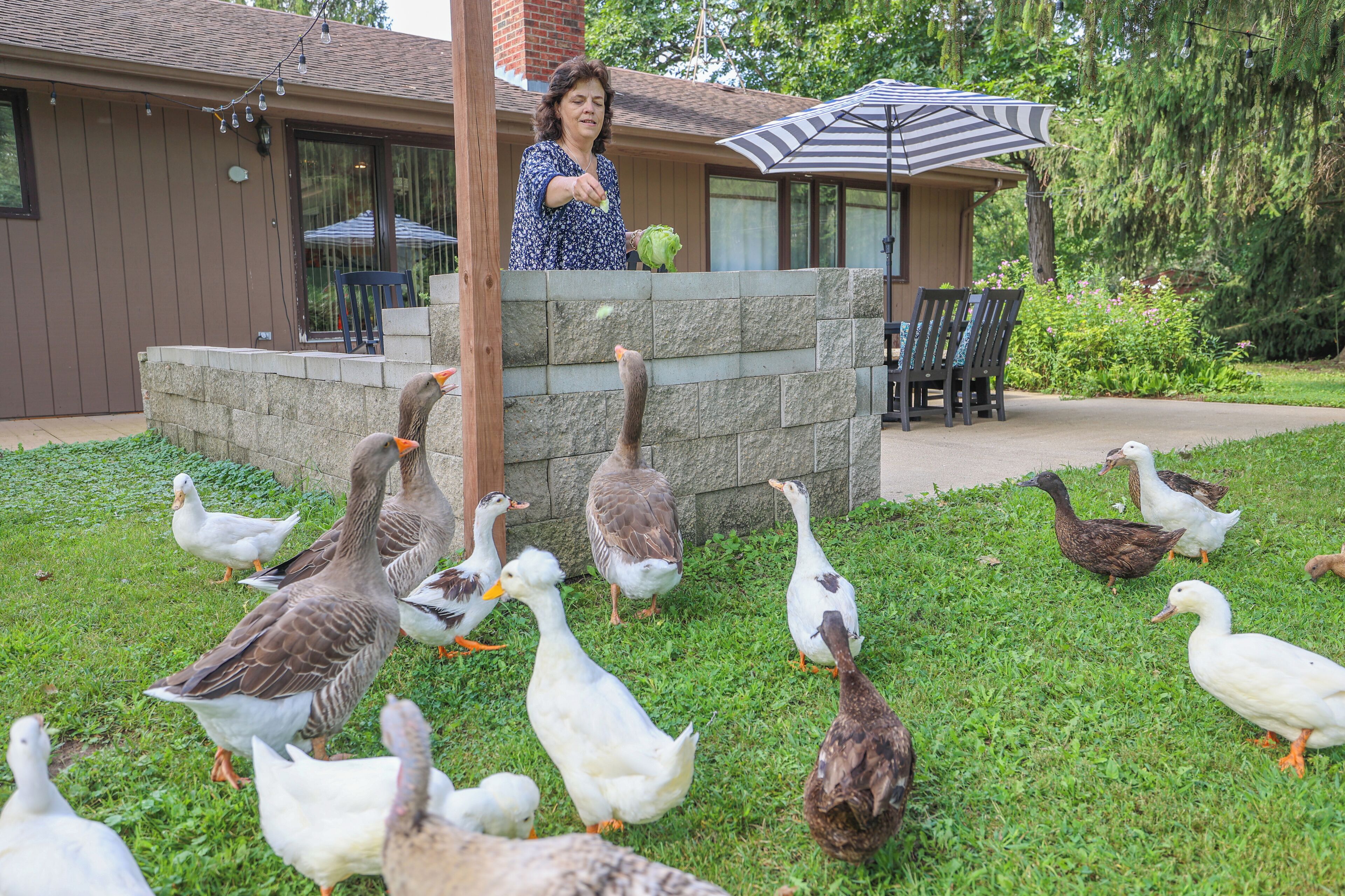 A patio area with a stone wall, outdoor furniture, and a woman standing by.