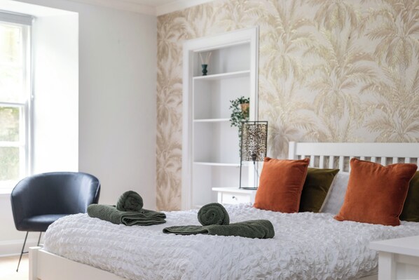 A neatly made bed with rolled towels, a white headboard, and a side table with a plant and a decorative item. - Charming, newly renovated 2 bedroom apartment in the heart of the city (Newington)