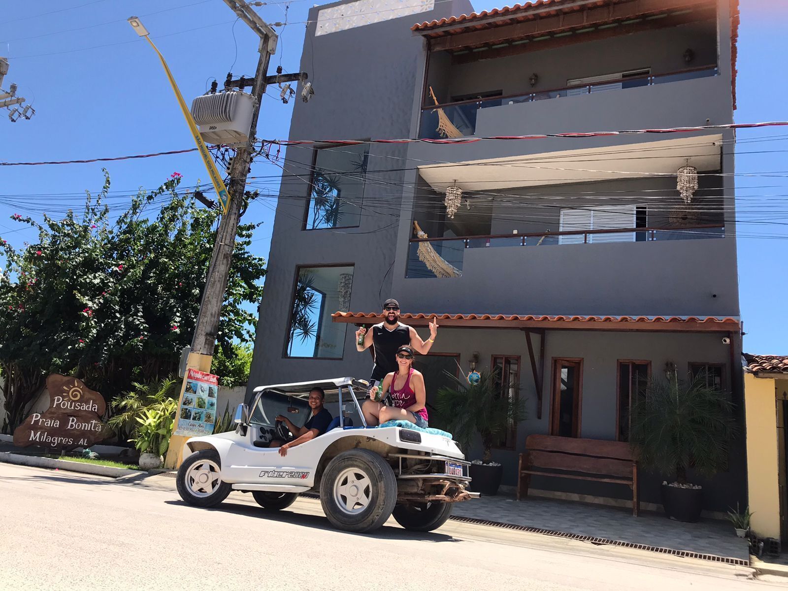 A white off-road vehicle parked in front of a building with a sign reading "Pousada Praia Bonita Milagres, AL".