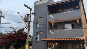 Un edificio de dos plantas con un balcón en el piso superior, un letrero en la fachada y un pequeño espacio al aire libre con mantel colorido.