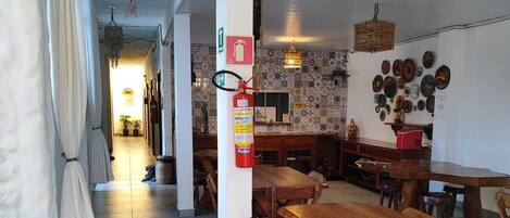 Un comedor amplio con mesas y sillas de madera, un extintor de incendios montado en la pared, y un salpicadero decorativo en la zona de la cocina.