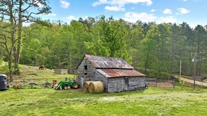 A rustic wooden barn with hay bales, a green tractor, and a cow grazing nearby. - The Highland Hideaway, perfect for family getaways (Piercetown)