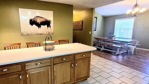 A kitchen with wooden cabinets, a white countertop, and a dining area with a table and chairs. - The Highland Hideaway, perfect for family getaways (Piercetown)