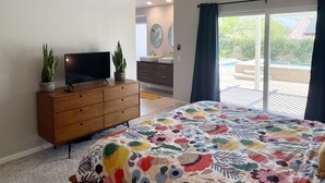 A bedroom with a bed, a TV on a wooden dresser, a bathroom with a sink and mirror, and a view of a pool outside. - 3bed 2bath House.  Private Pool and Spa. Close to Acrisure Center  (Indian Wells)