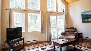 A spacious living room with large windows, a flat-screen TV, a sofa, and a coffee table. - Mountain Getaway and Family Retreat (Woodland Park)