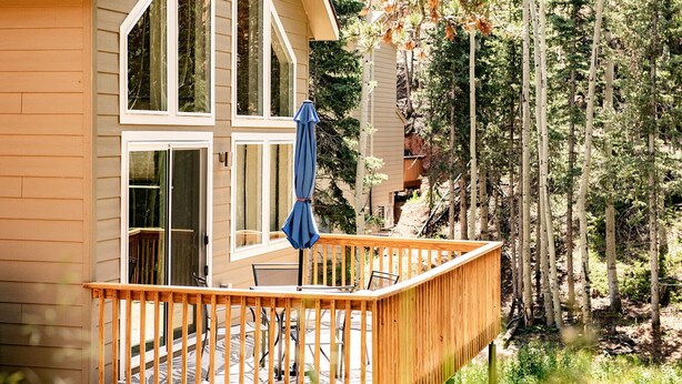 A wooden deck with a blue umbrella, a glass door, and a view of a forested area. - Mountain Getaway and Family Retreat (Woodland Park)