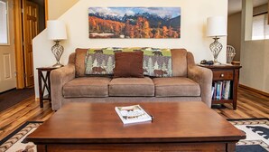 A living room with a brown sofa, a coffee table, and a painting of a mountainous landscape. - Mountain Getaway and Family Retreat (Woodland Park)