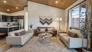 Una sala de estar moderna con techo de madera, un conjunto de sofá, una mesa de centro y un ventanal con cortinas.