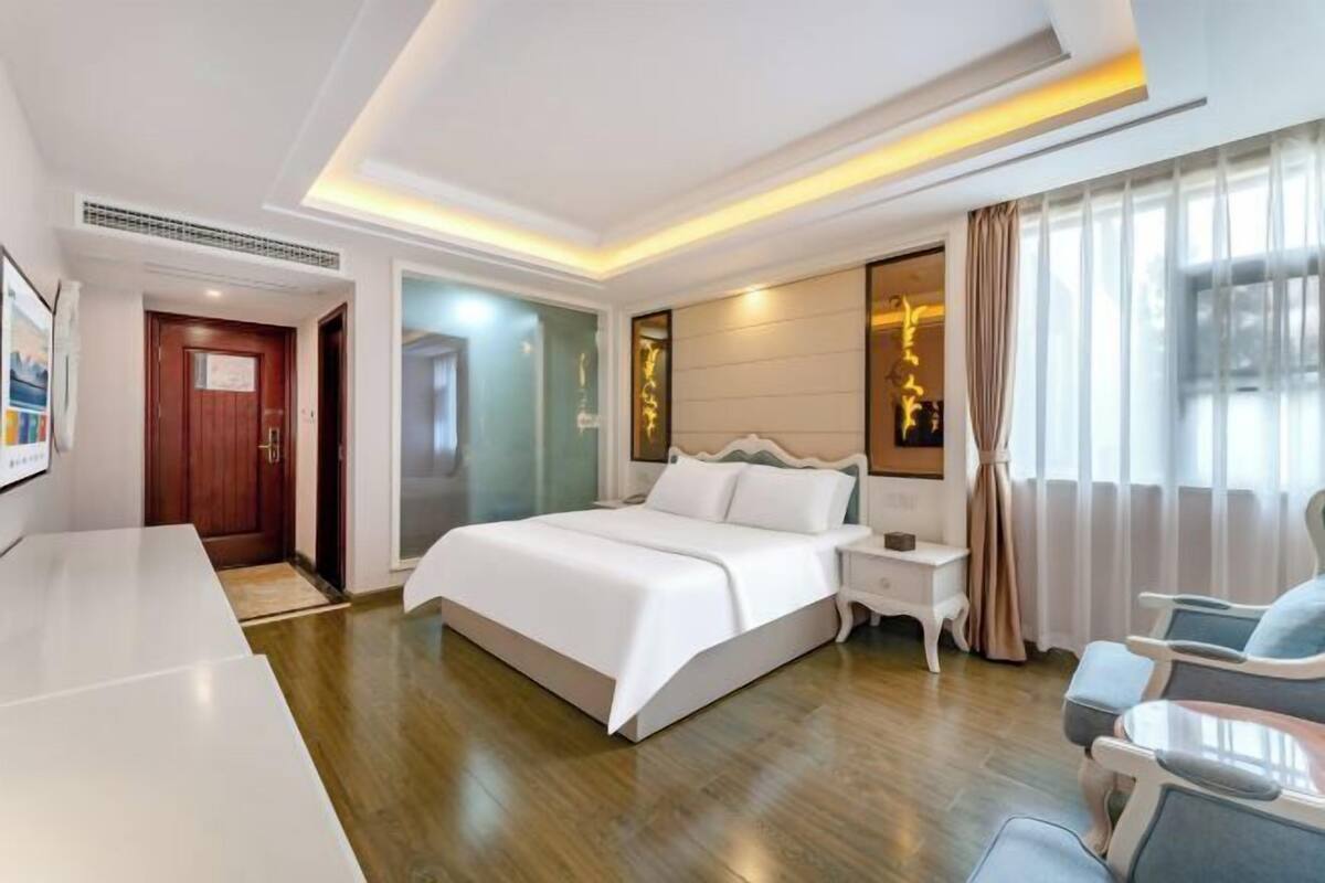 Quarto de hotel moderno com uma cama grande, mesas de cabeceira, uma escrivaninha e um espaço de estar.