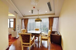 A hotel room with a dining area featuring a round table and four chairs, a sofa, and a large window with vertical blinds. - TianQuan Tianyi Jiacheng Hotel (Tianquan)