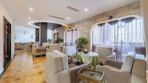 A modern lounge area with comfortable seating, a stone accent wall, and large windows with curtains. - TianQuan Tianyi Jiacheng Hotel (Tianquan)