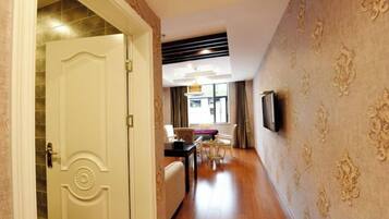 A hotel hallway with a closed door, a dining area with a table and chairs, and a wall-mounted television.