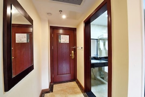 A hallway with a wooden door, a mirror, and a bathroom visible through a glass door. - TianQuan Tianyi Jiacheng Hotel (Tianquan)
