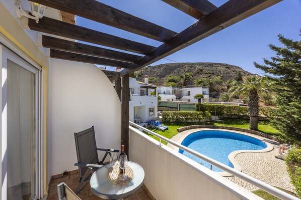 Un balcon donnant sur une piscine, avec une chaise et une table sur laquelle se trouvent une bouteille et un verre.