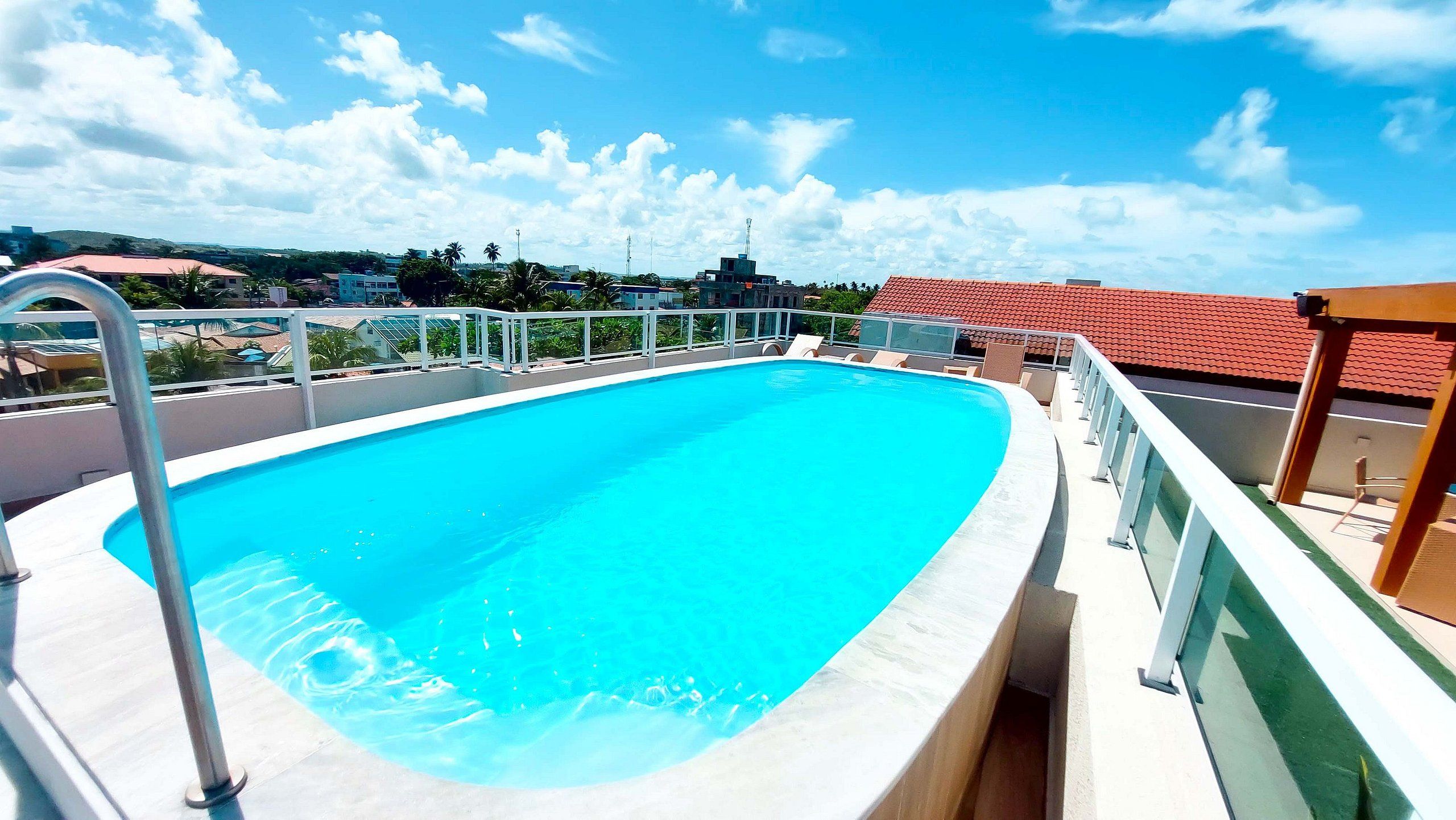 A rooftop swimming pool with a clear blue pool, a metal ladder, and a railing.
