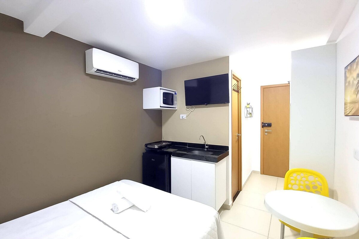 A compact room with a bed, a small kitchenette, a microwave, a TV, and a door leading to another room.