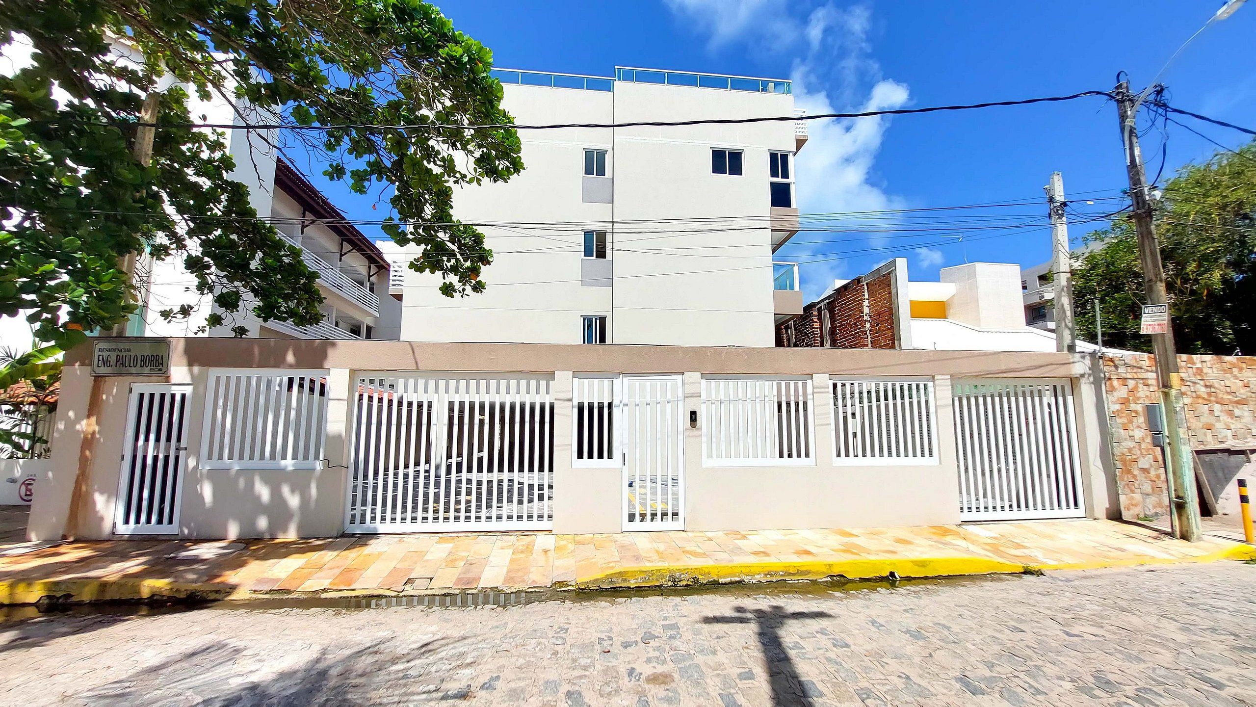 A residential building with a gated entrance, a sign indicating a sale, and a clear blue sky in the background.