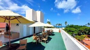 A rooftop terrace with outdoor seating, umbrellas, and a view of the ocean. - Residencial Engenheiro Paulo Borba (Ipojuca)