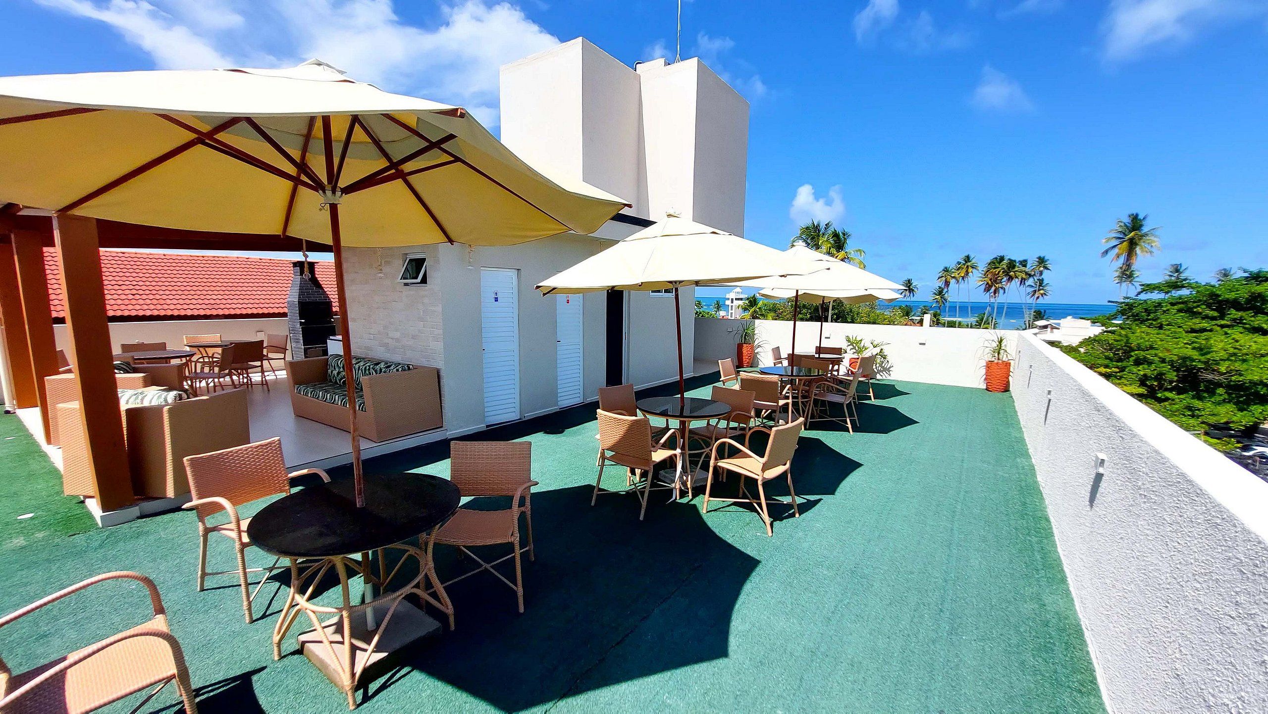 A rooftop patio with outdoor seating, umbrellas, and a view of the ocean.