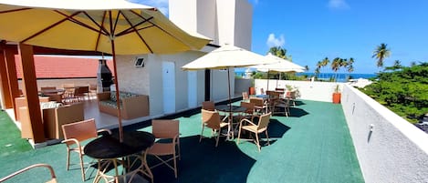 A rooftop patio with outdoor seating, umbrellas, and a view of the ocean.